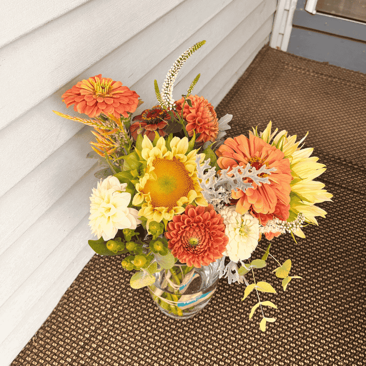 white sunflowers with pastel orange zinnia arrangement on a doorstep to be delivered